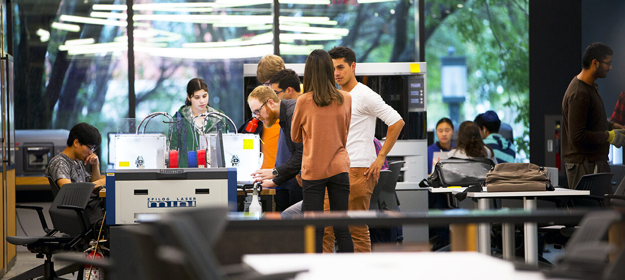 Students working and talking around a table with laptops.