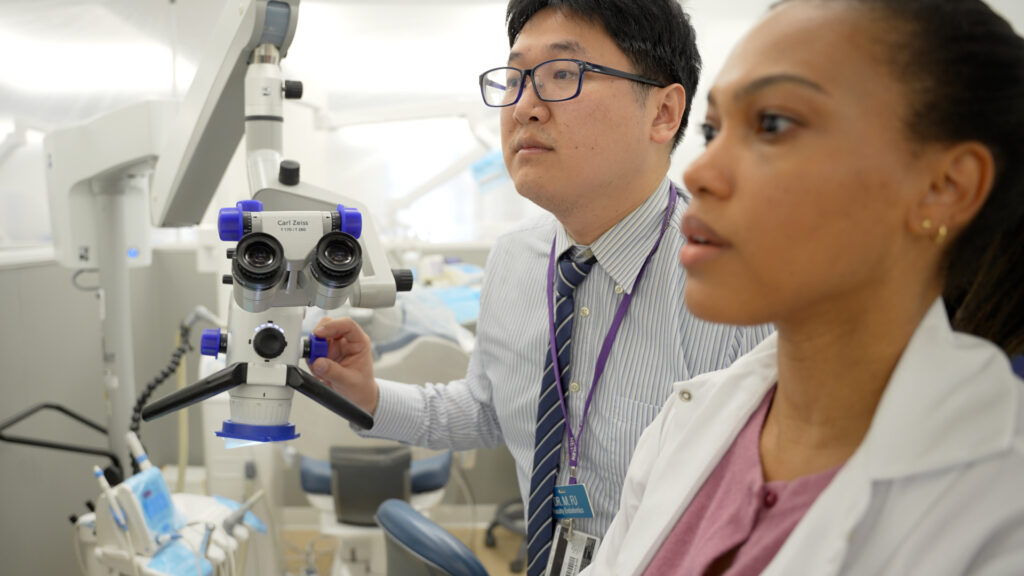 Two dental faculty members look at footage on a digital microscope.